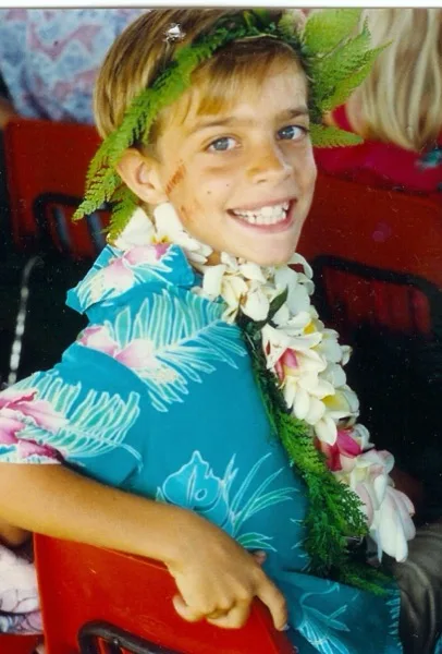 Cody as a kid on Kauaʻi, wearing a flower lei and fern crown at a May Day celebration.